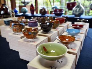 真右エ門窯による一点作ぐい呑みの集合体。辰砂の生命的な赤、藍染水滴の静謐な青、耀変天目の深淵な黒など、石の理性が1300度の炎の奇跡と出会い生まれた多様な「小宇宙」が並列している様。これらは単なる酒器の羅列ではなく、現代人の異なる魂の渇きを癒やし、精神を整える聖域（セラピー）としての選択肢が提示されている光景である。